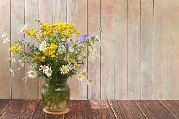 Floral arrangement of wild herbs and flowers on a wooden tabletansy, mint, celandine, chamomile and yarrow in a jar, collection of useful herbs for treatment according to folk recipes.