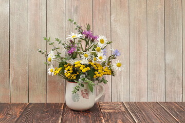 Floral composition of wild herbs and flowers, autumn background, tansy, mint, celandine, chamomile and yarrow in a mug on an old background, collection of useful herbs 