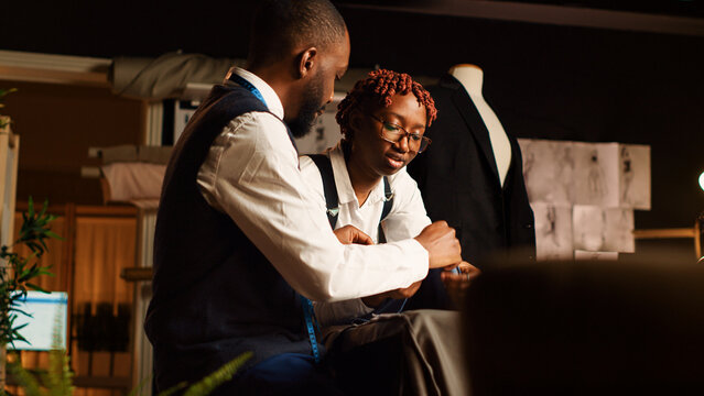 Designers reviewing material for items in atelier, choosing professional fabric on workstation before creating clothing line. Team of tailors manufacturing clothes with tools. Handheld shot.