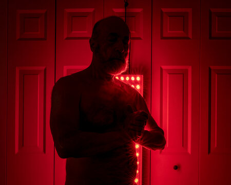 silhouette of a senior athletic, man torso standing in front of the red light therapy panel, home setup for treatment - Powered by Adobe