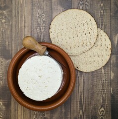 Mexican panela cheese in clay dish, two corn toasts, cutter on wooden table