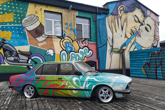 Irkutsk,Russia-July 17,2022:Conceptual background of street art.An old BMW car with colorful graffiti drawings on the background of a wall decorated with graffiti.Modern  urban culture of street youth
