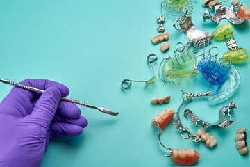 Hand of a dental technician wearing a purple glove with different dental orthodontic appliances.