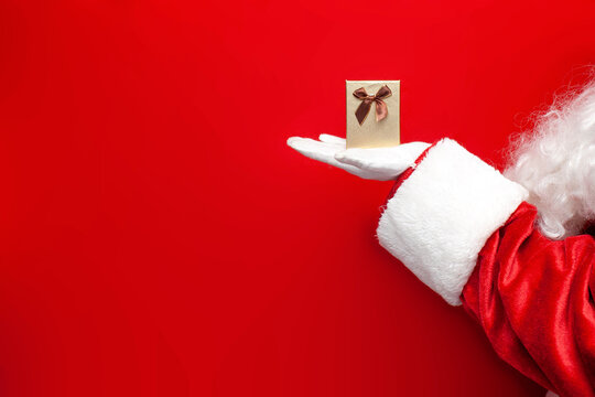 small gift box in the hands of santa claus on red background, santa gives festive gift for the new year - Powered by Adobe
