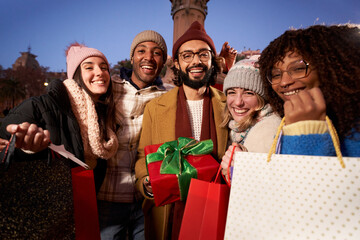 Portrait of group smiling multi-ethnic people showing Christmas winter shopping bags and gifts to camera. Photo happy young millennial friends posing cheerful outdoor. Relationships in community.