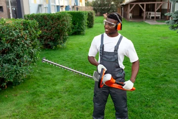 Selbstklebende Fototapete Grün portrait of garden worker in uniform with electric tool, african american man in protective glasses