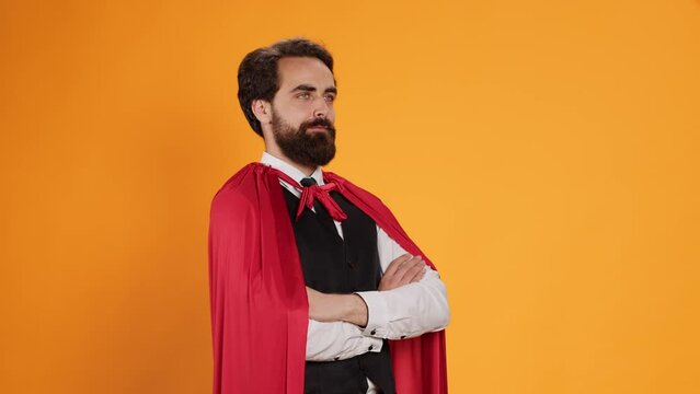 Powerful fantasy hero with red cape standing against yellow background, feeling determined and confident on camera. Dedicated butler acting like superhero, staff member having mantle.