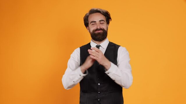 Passionate waiter applauds with both hands in studio to congratulate someone on recent performance. Young man cheering while he serves as butler in food establishment, confidence boost.
