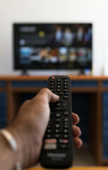 Vertical photo of a hand holding a television remote control while searching for a movie on television
