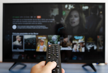 Hand holding a remote control while putting a serie on television