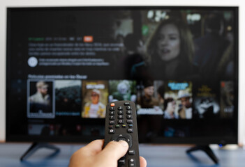 Fototapeta premium Hand holding a remote control while putting a serie on television