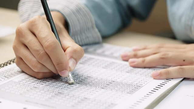 University students in uniform in classroom,Selective focus of the teenage college students sit on lecture chairs do final examination and write on examination paper answer sheets in the classroom. 