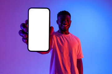 african american man showing empty smartphone screen in neon lighting, guy advertising copy space...