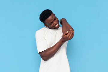 african american man hit his elbow and touches sore joint on his arm on blue isolated background