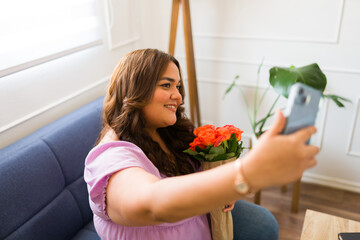 Beautiful woman taking a selfie with her phone after receiving romantic flowers