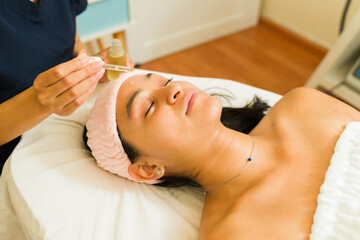 Obraz na płótnie Canvas Latin woman doing her skincare and using moisturizing serum