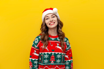 young beautiful girl in christmas clothes and santa hat smiles on yellow isolated background