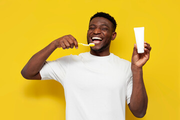 joyful african american man brushing his teeth and holding toothbrush and tube of toothpaste