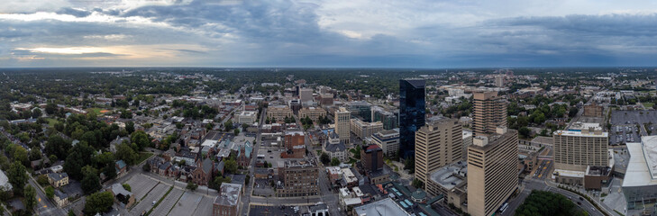 Drone panorama of the skyline of Lexington, Kentucky, displays the financial business district in the foreground and the University of Kentucky campus in the distance, set against a cloudy sunrise.
