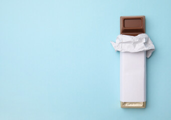 Tasty chocolate bar in package on light blue background, top view. Space for text