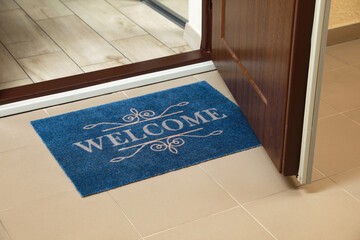 Beautiful blue doormat with word Welcome on floor near entrance