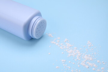 Bottle and scattered dusting powder on light blue background. Baby cosmetic product