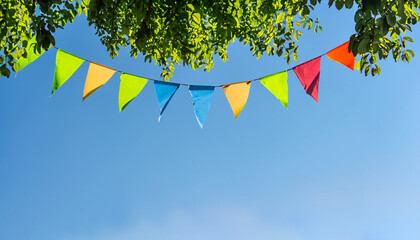 colorful pennant string decoration in green tree foliage on blue sky, summer party background...
