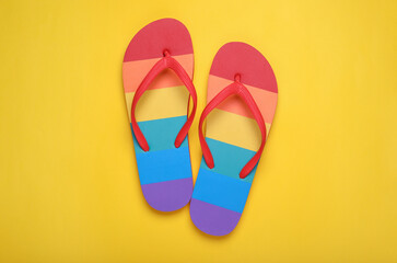 Rainbow flip flops on yellow background, flat lay. LGBT pride
