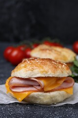 Delicious bagel with ham and cheese on dark grey textured table, closeup
