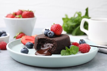Plate with delicious chocolate fondant, berries and mint on grey table, closeup