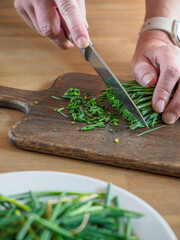 Woman hands cutting green fresh organic chives on wooden cutting board. Closeup.