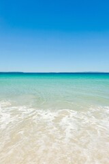 Fototapeta na wymiar Clear turquoise waters, cloudless blue skies, sea foam and white sand on a sunny day at Callala Beach in Shoalhaven — Jervis Bay National Park, New South Wales, Australia