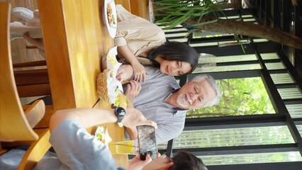 Asian man using mobile phone taking picture his wife and elderly father during having lunch eating food together at restaurant on summer vacation. Family relationship old people health care concept. - Powered by Adobe