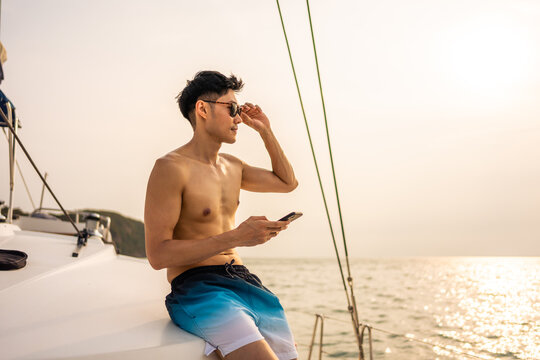 Asian young man tourist using smartphone chat online during yachting. 