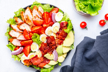 Traditional Cobb salad with chicken fillet, tomatoes, eggs, bacon, avocado and lettuce, gray table background, top view. American cuisine dish