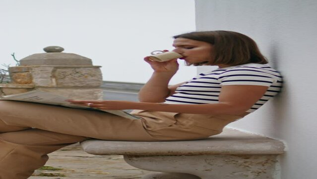 Woman reading morning newspaper on terrace vertical. Relaxed girl drink coffee