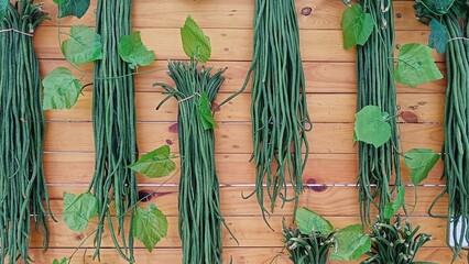 Various green long bean vegetables are hung and arranged neatly on the wooden wall