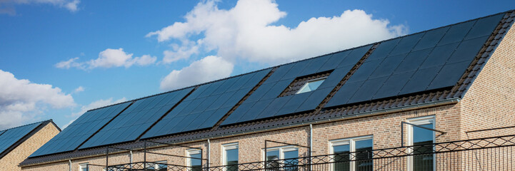 Fototapeta premium Newly build houses with solar panels attached on the roof against a sunny sky , Close up of new building with black solar panels in the Netherlands