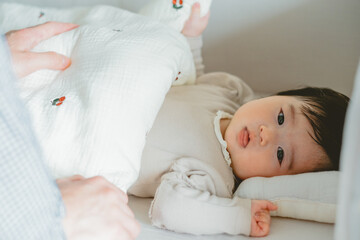 Obraz na płótnie Canvas 秋の午後、ベビーベッドで布団を掛けて寝そべる遠くを見つめるアジア人の赤ん坊