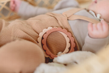 春の日中、ゆりがこで横たわる赤ちゃんの横に置かれた花形の歯固めのおもちゃ - obrazy, fototapety, plakaty