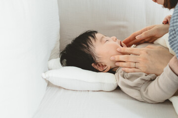 Obraz na płótnie Canvas 春の日中、ベビーベッドで横たわり母親にほっぺを触れられる日本人の黒髪の赤ちゃん
