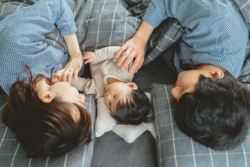 春の朝、布団で寝転がる日本人の父親と母親と赤ちゃんの3人家族