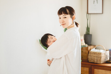 春の日中、リビングで眠る赤ちゃんを抱っこして立つアジア人の30代女性