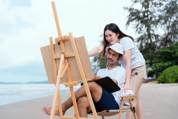 Young couple relaxing by the sea in the morning sit and paint with watercolors as a hobby
