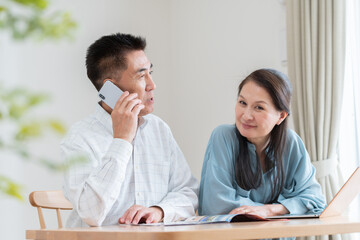 旅行パンフレットを見て予約をするシニア夫婦