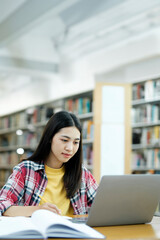 Young university student using laptop for online learning, searching and learning at library.