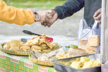 Female buyer giving money to seller while buying Gorengan Fries on market. A customer paying with physical paper money on street food stall.