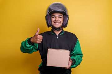 Asian online motorbike taxi driver wearing green jacket and helmet while holding to a package and giving thumbs up