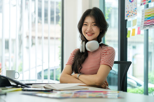 Smiling asian female graphic designer wearing headphone sitting front of computer sat her office..