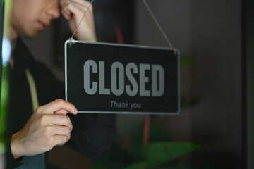 Cropped shot of male entrepreneur turning Closed sign on the entrance door of his small cafe. Financial difficulties and economic crisis.